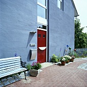 Bank auf der Terrasse eines modernen grauen Hauses mit roter Tür