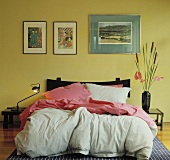 Bilder über dem Bett mit rosa Kissen und Bettdecken in einem modernen gelben Schlafzimmer