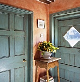 Ecke im Vorraum mit blaugrauen Türen und orangeroter Wand mit Blumenvase auf rustikalem Blumenständer