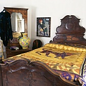 Antikes Bett mit Kopfteil aus dunklem Holz und goldfarbener Tagesdecke mit orientalischem Motiv