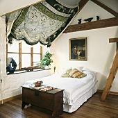 Schlichtes Schlafzimmer unter dem Dach mit antiker Truhe am Bettende und darüber gespannter Stoff