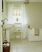 Ländliches weisses Badezimmer mit Standwaschbecken und Stuhl vor Fenster
