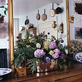 Lila Hortensien und Blätter in Kupferkrug vor großem vergoldetem Spiegel