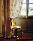 Stuhl am Fenster mit geblümten Vorhang im Landhausstil