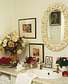 Ovaler Spiegel mit Rahmen aus Muscheln über Waschtisch mit verschiedenen Blumensträusse in Vase