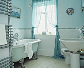 Modernes Badezimmer mit freistehender Badewanne im Vintagelook vor hellblauer Wand