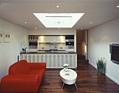 Offener Wohnraum mit rotem Sofa und weißem Couchtisch vor offener Küche und Parkett