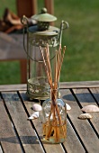Incense stick in a glass bottle in front of an antique lantern on wooden boards
