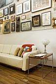 A white, modern sofa with a side table and a collection of pictures on the wall