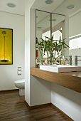 A contemporary bathroom with a wash basin set into a wooden counter and a plant in front of a mirror