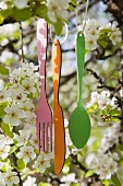 Decorative cutlery hanging from strings in a flowering apple tree
