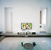 A glass coffee table, a low sideboard with multimedia devices inside and a flat-screen television on the wall