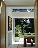 A view through an open doorway in a modern apartment through open terrace doors onto a garden