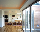 Offener Wohnraum mit farbigem indirektem Deckenlicht und Terrassentüren vor rustikalem Essbereich