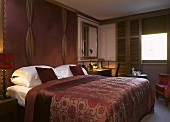 Bedroom with elegant gold and red bedspread on double bed against wall covered in leather