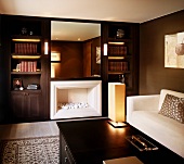 Klassisch moderner Herren-Wohnraum mit weißem Sofa vor dunkelbraunen Wänden und Kamin neben Einbauregalschränken