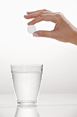 A hand holding an effervescent tablet over a glass