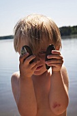 Little boy on a lakeside holding two shells in his hands