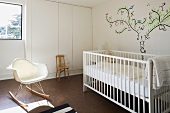 Babyzimmer mit weißem Gitterbett, Wandmalerei & Schaukelstuhl