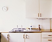 weiße Küche mit Spülbecken aus Edelstahl und Bahnhofsuhr