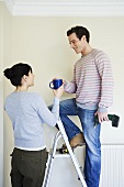 A woman giving a cup of coffee to a man on a stepladder