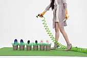 A woman watering shoes in flower pots with a hosepipe