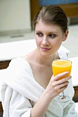 Young woman in bathrobe drinking orange juice