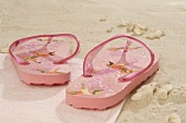 Pink flip-flops on a towel on sand