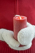 Hands in mittens holding burning candle