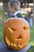 Carved pumpkin face for Halloween, child in background