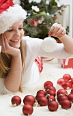 Woman in Father Christmas hat lying on carpet with Xmas baubles