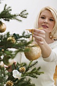 Woman hanging gold bauble on Christmas tree