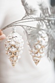Hand holding Christmas decoration (silver cones on branch)