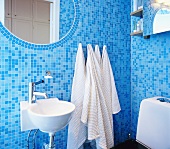 Badezimmer mit blauen Mosaikfliesen und einem eingelegten, ovalen Spiegel