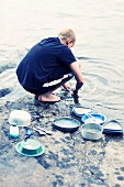 Junge wäscht das Geschirr am Fluss ab
