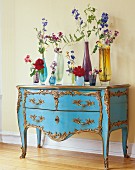 Various vases of flowers on blue chest of drawers