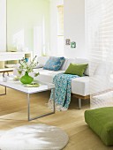 A light-flooded, white living room with a sofa, coffee table and touches of green and blue