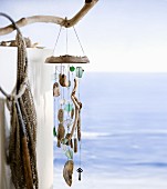Künstlerisch gestaltetes Windspiel aus Naturfundstücken an Ast aufgehängt, im Hintergrund das Meer