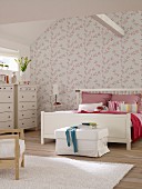 White double bed and chests of drawers in bedroom with pink and white floral wallpaper and ceiling beam