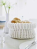 A white crochet bread basket filled with fresh rolls