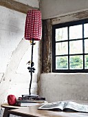 Tischleuchte mit rot-weiss kariertem Schirm und Metallfuss auf Tisch vor Sprossenfenster in rustikalem Ambiente