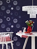 White chair and table with strawberries and flowers in front of blue, printed wallpaper