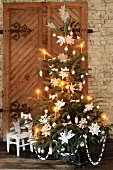 A Christmas tree in front of a rustic wooden door decorated with nostalgic paper stars and candles