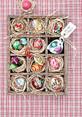 Colourful, hand-painted Easter eggs in a seedling tray lined with straw (seen from above)