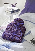 A knitted hot water bottle cover made from purple pom-pom yarn
