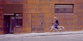 Lady riding a bike past a house facade with rusty Corten steel siding