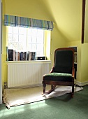 A green upholstered rocking chair in reading corner by a window