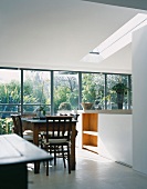 Dining table with chairs made of dark wood in a open-plan, modern kitchen with large bank of windows