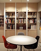 Round dining table and colored shell chairs in Bauhaus style in front of a built-in book shelf