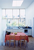 Rosa Tischdecke auf Esstisch mit rustikalen Stühlen in offener weisser Küche